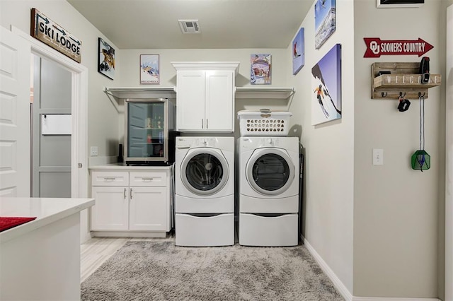 laundry area featuring cabinet space, baseboards, visible vents, washer and clothes dryer, and light wood-style flooring