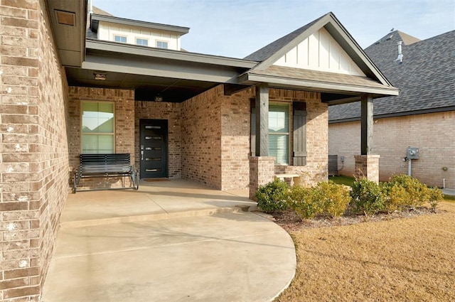 property entrance featuring a shingled roof, board and batten siding, and brick siding