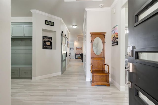 corridor featuring light wood-type flooring, a barn door, ornamental molding, and baseboards