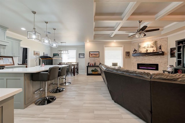 living area featuring ceiling fan, a stone fireplace, coffered ceiling, ornamental molding, and beamed ceiling