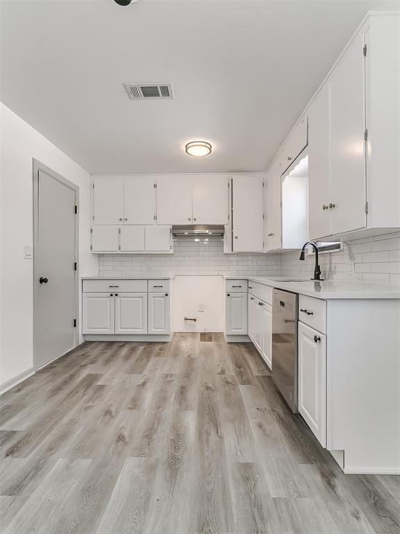 kitchen featuring visible vents, decorative backsplash, stainless steel dishwasher, a sink, and under cabinet range hood