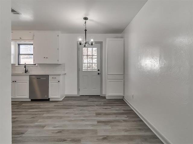 kitchen with white cabinetry, stainless steel dishwasher, a wealth of natural light, decorative backsplash, and light wood finished floors