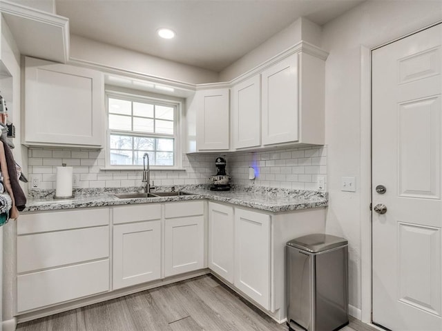 kitchen featuring white cabinets, light wood-style flooring, light stone counters, a sink, and backsplash