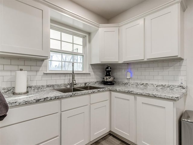 kitchen with wood finished floors, backsplash, a sink, and white cabinetry