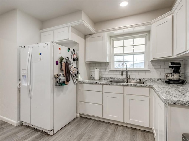 kitchen featuring light wood-style flooring, white fridge with ice dispenser, decorative backsplash, and a sink
