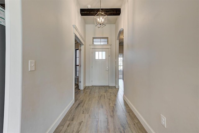 doorway to outside with arched walkways, light wood-style flooring, baseboards, beamed ceiling, and an inviting chandelier