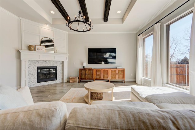 living area with a fireplace, an inviting chandelier, ornamental molding, light wood-type flooring, and beamed ceiling