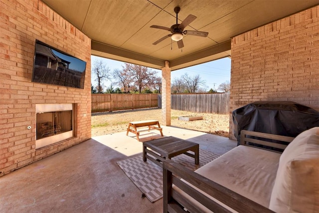 view of patio with an outdoor brick fireplace, area for grilling, a fenced backyard, and a ceiling fan