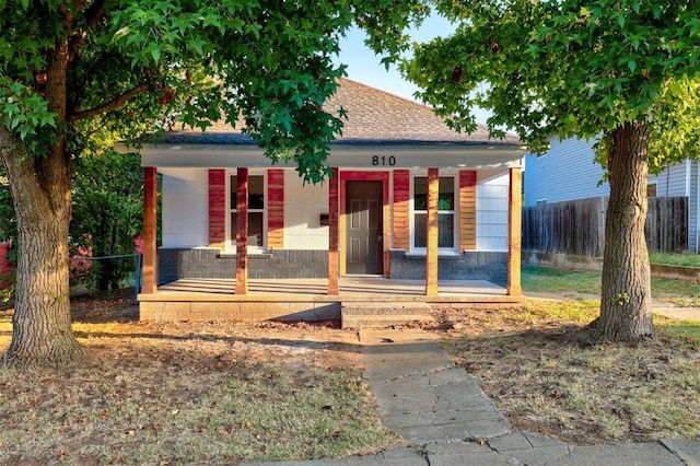 view of front facade featuring a shingled roof, fence, and a porch