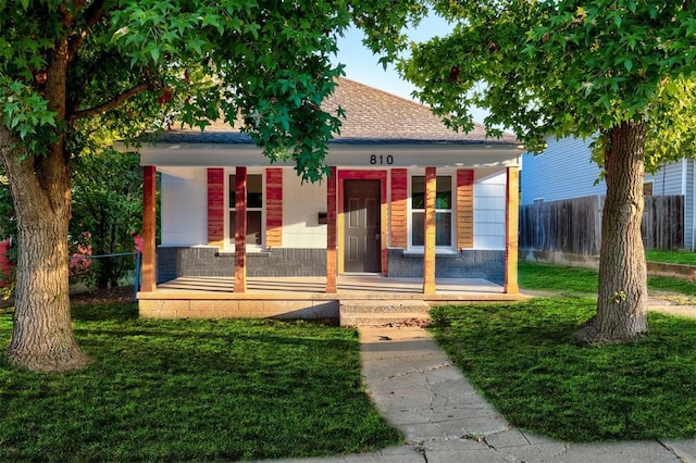 view of front facade featuring covered porch, a front lawn, roof with shingles, and fence