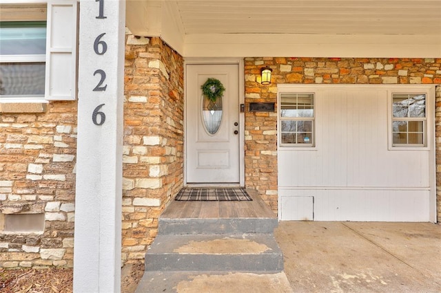 doorway to property with a porch, stone siding, and brick siding