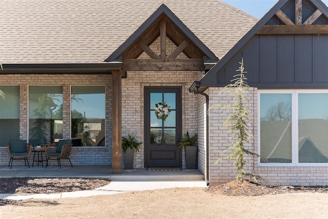 property entrance with a shingled roof, covered porch, brick siding, and board and batten siding