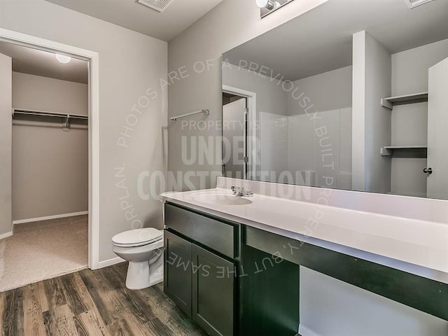 full bath with toilet, wood finished floors, vanity, baseboards, and a walk in closet