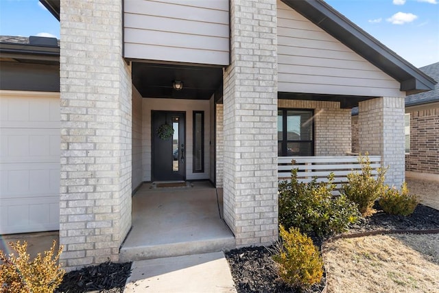 doorway to property with covered porch, brick siding, and an attached garage