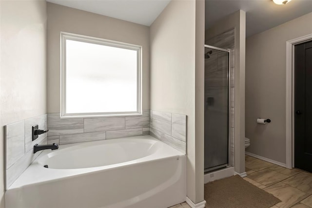 bathroom with a stall shower, a garden tub, toilet, and baseboards