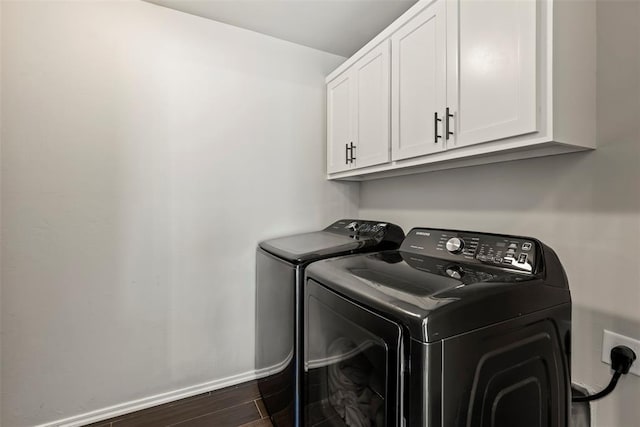 clothes washing area featuring dark wood-type flooring, washer and clothes dryer, cabinet space, and baseboards