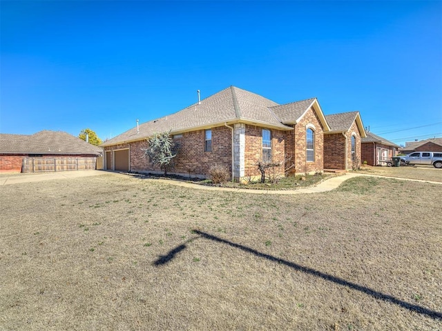 view of home's exterior with a garage, driveway, a shingled roof, a lawn, and brick siding