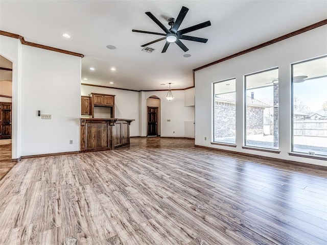 unfurnished living room with arched walkways, light wood finished floors, plenty of natural light, and visible vents