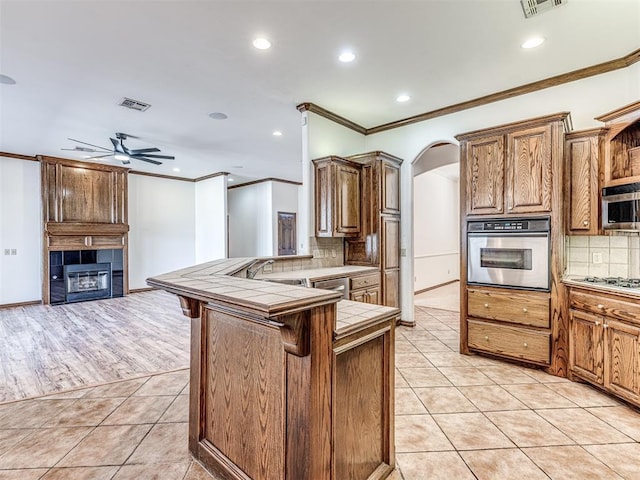 kitchen with light tile patterned floors, tile counters, appliances with stainless steel finishes, a peninsula, and a kitchen bar