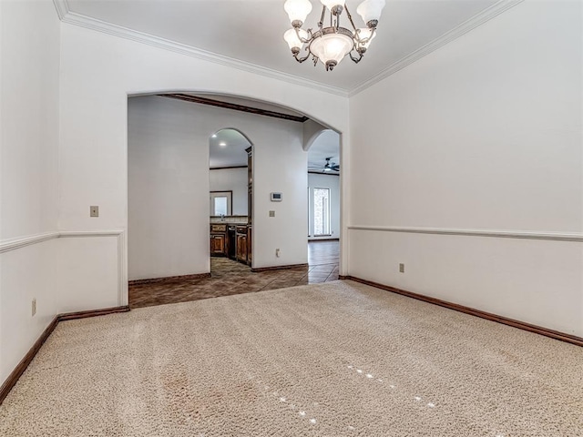 carpeted spare room with arched walkways, ceiling fan with notable chandelier, baseboards, and crown molding