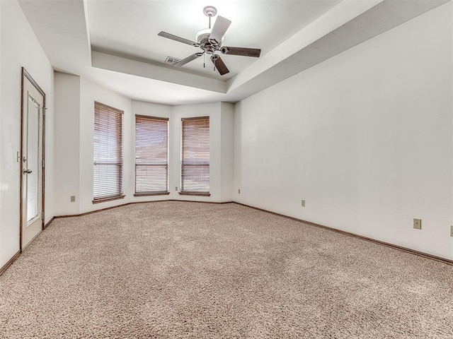 carpeted spare room featuring a ceiling fan, visible vents, a tray ceiling, and baseboards