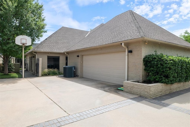 view of side of home with driveway, a shingled roof, an attached garage, fence, and central air condition unit