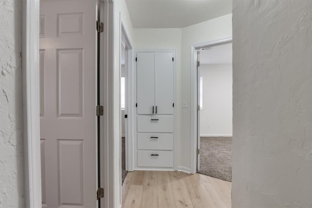 corridor featuring light wood-style flooring, baseboards, and a textured wall