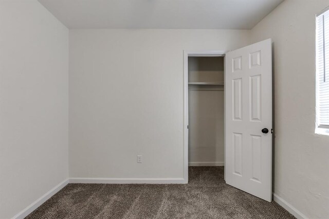 unfurnished bedroom with dark colored carpet, a closet, multiple windows, and baseboards