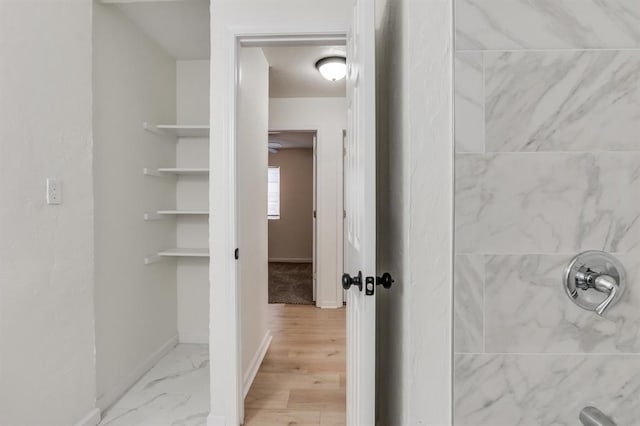 bathroom featuring marble finish floor, a tile shower, and baseboards