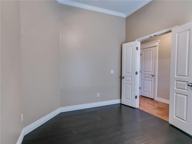 spare room featuring dark wood-style floors, crown molding, and baseboards