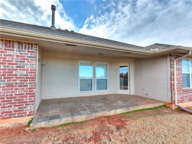 back of property featuring brick siding, a patio, and roof with shingles