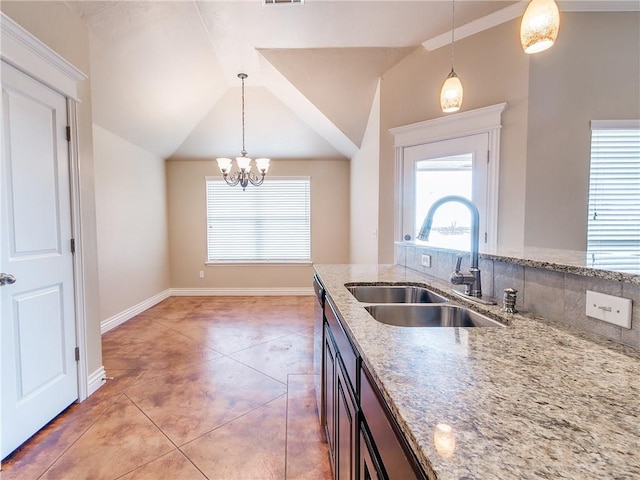 kitchen with lofted ceiling, a sink, decorative light fixtures, and light stone countertops