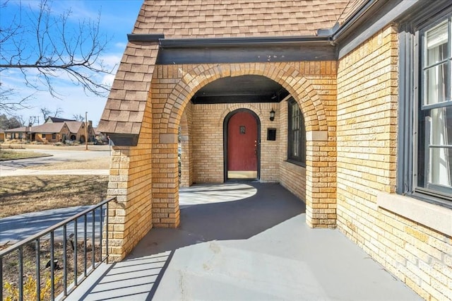 doorway to property with a shingled roof, brick siding, and a porch