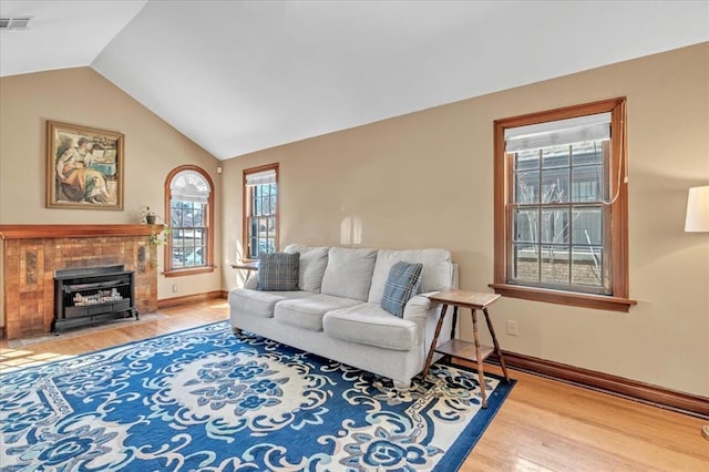 living area featuring visible vents, a fireplace with flush hearth, vaulted ceiling, wood finished floors, and baseboards