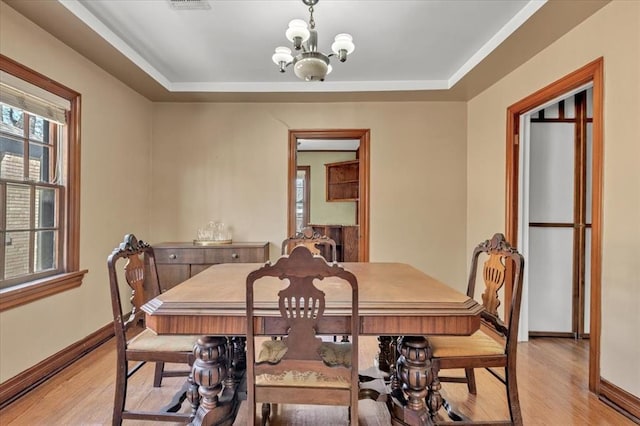 dining room with baseboards, a tray ceiling, light wood-style flooring, and a notable chandelier