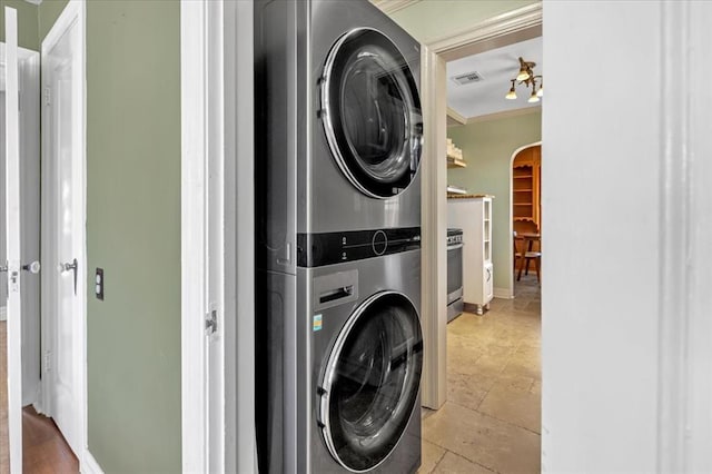 clothes washing area featuring laundry area, visible vents, arched walkways, stacked washer and clothes dryer, and ornamental molding