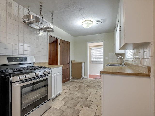 kitchen featuring visible vents, backsplash, stainless steel gas stove, white cabinetry, and a sink