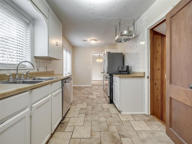 kitchen featuring tasteful backsplash, light countertops, stainless steel appliances, white cabinetry, and a sink