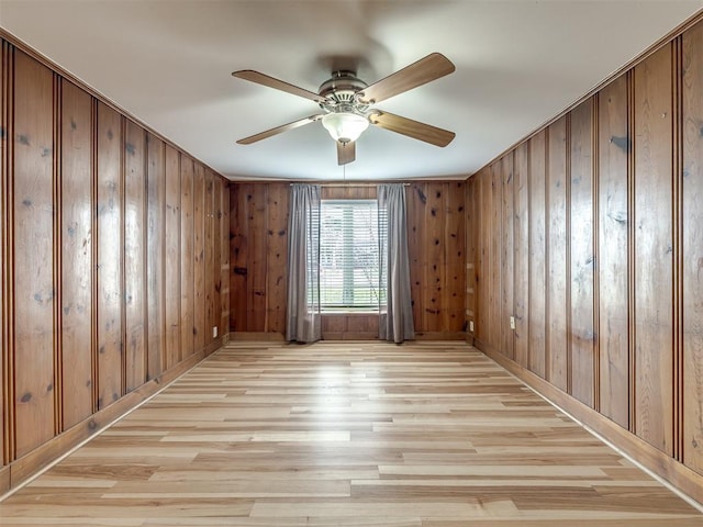 spare room with light wood-type flooring, wood walls, and ceiling fan