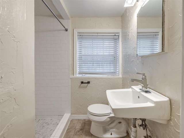 full bath featuring a sink, tiled shower, toilet, and a textured wall