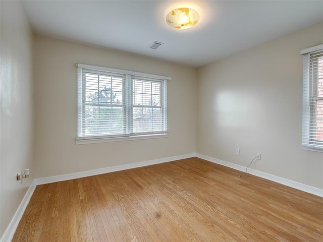 spare room featuring light wood-type flooring, visible vents, plenty of natural light, and baseboards