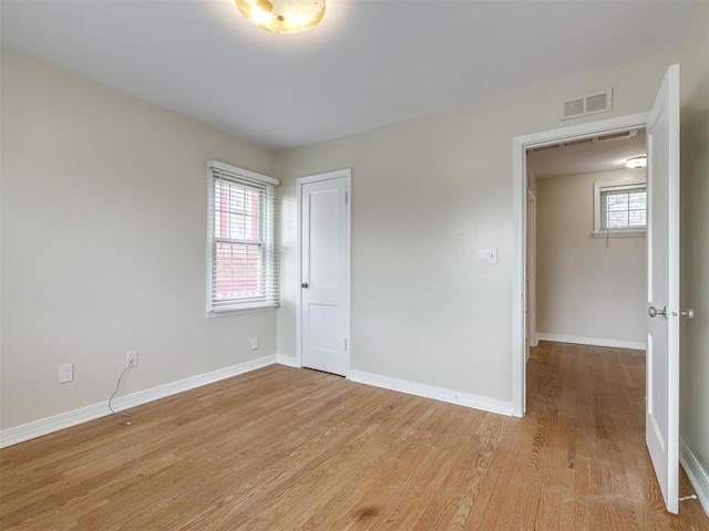 empty room featuring visible vents, plenty of natural light, light wood-type flooring, and baseboards