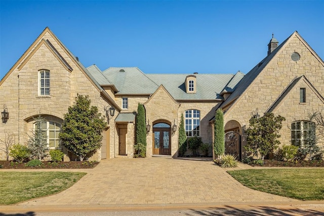 french country inspired facade with a garage, a front yard, decorative driveway, and french doors