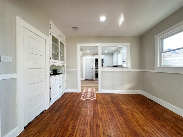 interior space featuring dark wood-type flooring, white cabinets, visible vents, and baseboards