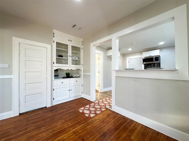 kitchen with dark wood-type flooring, visible vents, baseboards, white cabinets, and stainless steel microwave