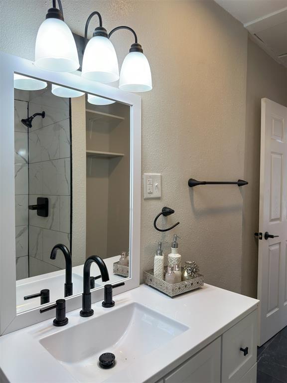 bathroom with a textured wall, a tile shower, and vanity