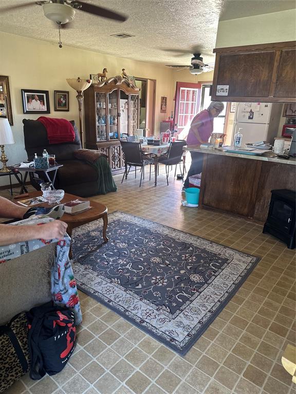 living room featuring tile patterned floors, visible vents, a textured ceiling, and a ceiling fan