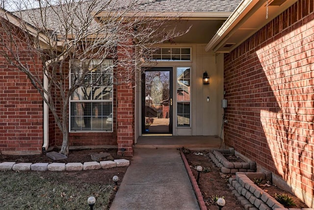 view of exterior entry with a shingled roof and brick siding