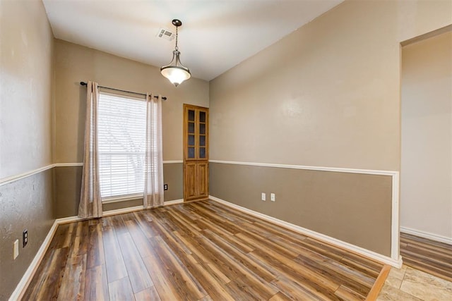 spare room featuring wood finished floors, visible vents, and baseboards