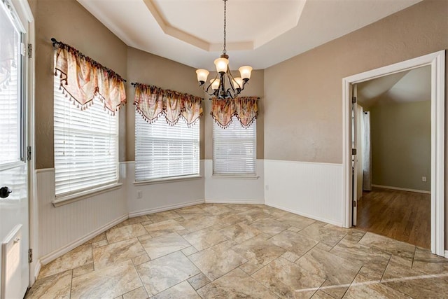 unfurnished dining area featuring a wainscoted wall, a raised ceiling, and a notable chandelier